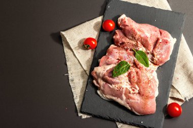 Çiğ hindi budu ve baharat. Seramik tezgahta taze kemiksiz et. Modern sert ışık, karanlık gölge. Siyah taş arkaplan, üst görünüm