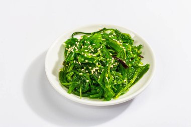 Chuka Seaweed salatası ve beyaz arka planda susam tohumları. Modaya uygun sert ışık, karanlık gölge. Model, şablon, düz uzanma
