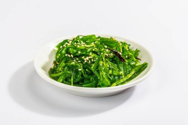 Chuka Seaweed salatası ve beyaz arka planda susam tohumları. Modaya uygun sert ışık, karanlık gölge. Model, şablon, düz uzanma