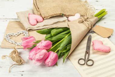 Bir buket taze pembe lale. Bahar çiçeği süslemesi yapıyorum. Aletler, antika makas, el işi kağıt, yumuşak kalpler. Beyaz tahta arka plan, kapat