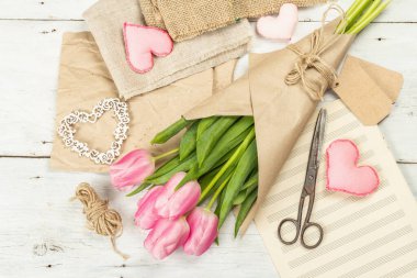 Bir buket taze pembe lale. Bahar çiçeği süslemesi yapıyorum. Aletler, antika makas, el işi kağıt, yumuşak kalpler. Beyaz tahta tahta arka plan, üst görünüm