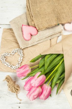 Bir buket taze pembe lale. Bahar çiçeği süslemesi yapıyorum. Aletler, antika makas, el işi kağıt, yumuşak kalpler. Beyaz tahta tahta arka plan, üst görünüm