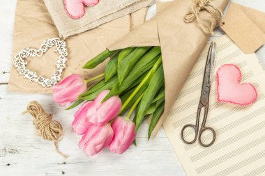 Bir buket taze pembe lale. Bahar çiçeği süslemesi yapıyorum. Aletler, antika makas, el işi kağıt, yumuşak kalpler. Beyaz tahta tahta arka plan, üst görünüm