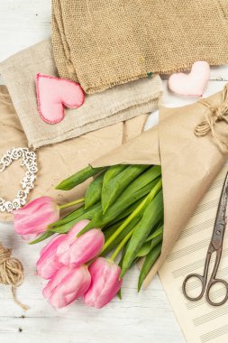 Bir buket taze pembe lale. Bahar çiçeği süslemesi yapıyorum. Aletler, antika makas, el işi kağıt, yumuşak kalpler. Beyaz tahta tahta arka plan, üst görünüm