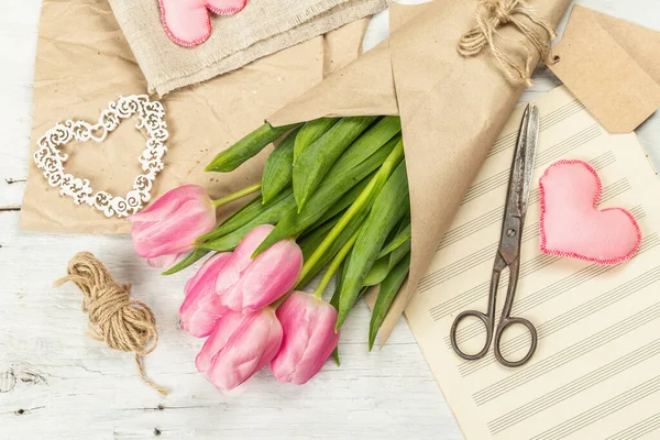 Bir buket taze pembe lale. Bahar çiçeği süslemesi yapıyorum. Aletler, antika makas, el işi kağıt, yumuşak kalpler. Beyaz tahta tahta arka plan, üst görünüm