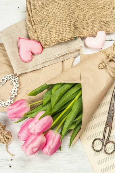 Bir buket taze pembe lale. Bahar çiçeği süslemesi yapıyorum. Aletler, antika makas, el işi kağıt, yumuşak kalpler. Beyaz tahta tahta arka plan, üst görünüm