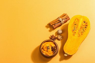 Çiğ balkabağının yarısı tereyağlı püre ve baharatlı. Yemek pişirmek için çeşitli malzemeler, açık turuncu arka plan, sert ışık, koyu gölge, üst görüş