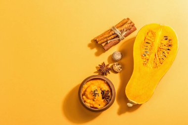 Çiğ balkabağının yarısı tereyağlı püre ve baharatlı. Yemek pişirmek için çeşitli malzemeler, açık turuncu arka plan, sert ışık, koyu gölge, üst görüş