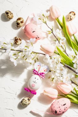 Çiçek açan kiraz, laleler ve şirin tavşanla Paskalya arkaplanız kutlu olsun. Bahar bayramı düzlüğü, geleneksel semboller, sert açık koyu gölge, beyaz macun arkaplan, kapat