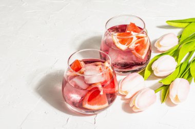 Greyfurtlu alkolsüz kokteyl. Bardakta buzlu içecek servis edilir. Sevgililer Günü sembolü bir kalp ve nazik lalelerdir. Sert ışık, karanlık gölge, beyaz ahşap zemin, kopyalama alanı