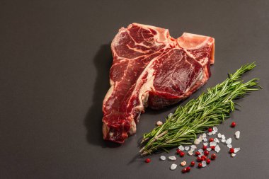 Siyah beton arka planda baharatlı klasik T-bone bifteği. Taze biberiye, modaya uygun sert ışık, koyu gölge, düz yer, kopyalama alanı