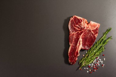Siyah beton arka planda baharatlı klasik T-bone bifteği. Taze biberiye, modaya uygun sert ışık, koyu gölge, düz yer, üst manzara