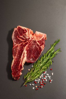 Siyah beton arka planda baharatlı klasik T-bone bifteği. Taze biberiye, modaya uygun sert ışık, koyu gölge, düz yer, üst manzara