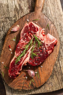 Taze biberiye, sarımsak ve baharatlı klasik biftek. Modern, sert bir ışık, karanlık bir gölge, modaya uygun bir duruş, ahşap arka plan, düz yatış. Ahşap arkaplan, köy tarzı, üst görünüm