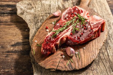 Taze biberiye, sarımsak ve baharatlı klasik biftek. Modern, sert bir ışık, karanlık bir gölge, modaya uygun bir duruş, ahşap arka plan, düz yatış. Ahşap arkaplan, rustik biçim, kopyalama alanı