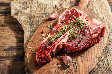 Taze biberiye, sarımsak ve baharatlı klasik biftek. Modern, sert bir ışık, karanlık bir gölge, modaya uygun bir duruş, ahşap arka plan, düz yatış. Ahşap arkaplan, rustik biçim, kopyalama alanı