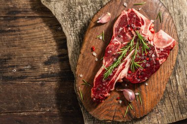 Taze biberiye, sarımsak ve baharatlı klasik biftek. Modern, sert bir ışık, karanlık bir gölge, modaya uygun bir duruş, ahşap arka plan, düz yatış. Ahşap arkaplan, köy tarzı, üst görünüm