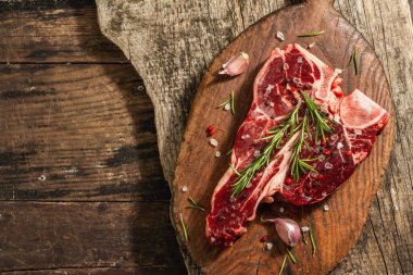 Taze biberiye, sarımsak ve baharatlı klasik biftek. Modern, sert bir ışık, karanlık bir gölge, modaya uygun bir duruş, ahşap arka plan, düz yatış. Ahşap arkaplan, köy tarzı, üst görünüm