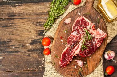 Taze biberiye, sarımsak ve baharatlı klasik biftek. Modern, sert bir ışık, karanlık bir gölge, modaya uygun bir duruş, ahşap arka plan, düz yatış. Ahşap arkaplan, köy tarzı, üst görünüm