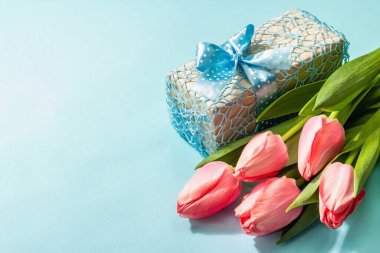 Kutlama konsepti çiçek kompozisyonu, bir buket pembe lale ve bir hediye. Uluslararası Kadınlar, Sevgililer Günü, ya da Anneler Günü, Düğün. Mavi arkaplan, düz yatış