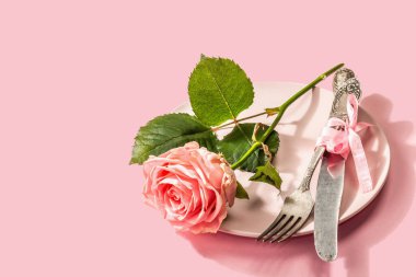 Gül arka planında izole edilmiş romantik yemek masası. Sevgililer günü ya da anneler günü için aşk konsepti, düğün çatal bıçak takımı. Narin pembe bir gül, masa seti.