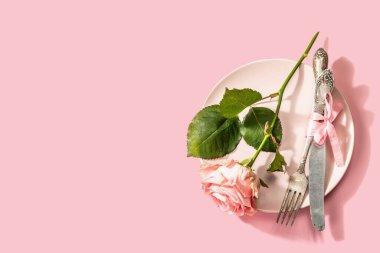Gül arka planında izole edilmiş romantik yemek masası. Sevgililer günü ya da anneler günü için aşk konsepti, düğün çatal bıçak takımı. Narin pembe bir gül, masa seti.