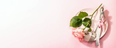 Gül arka planında izole edilmiş romantik yemek masası. Sevgililer günü ya da anneler günü için aşk konsepti, düğün çatal bıçak takımı. Narin pembe bir gül, tablo ayarı, pankart biçimi