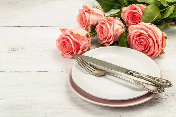 白い木製の背景にロマンチックなディナーテーブル バレンタインや母の日 結婚式のカトラリーのための愛の概念 新鮮なピンクのバラの花束 テーブル設定 コピースペース — ストック写真