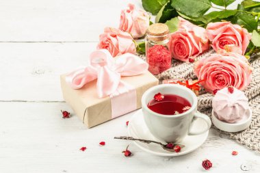 Romantik çay kavramı. Paketlenmiş hediye, amber çayı, bir buket narin gül, şeker, şenlikli dekor. Sevgililer Günü konsepti, Kadınlar Günü 8 Mart, Düğün. Beyaz pano arkaplanı, kopyala