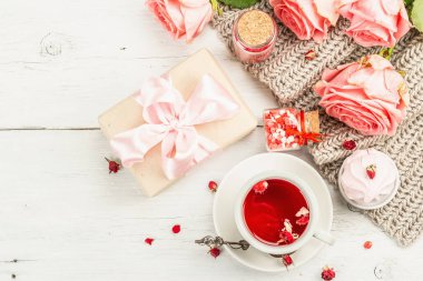 Romantik çay kavramı. Paketlenmiş hediye, amber çayı, bir buket narin gül, şeker, şenlikli dekor. Sevgililer Günü konsepti, Kadınlar Günü 8 Mart, Düğün. Beyaz tahta arkaplan, üst görünüm