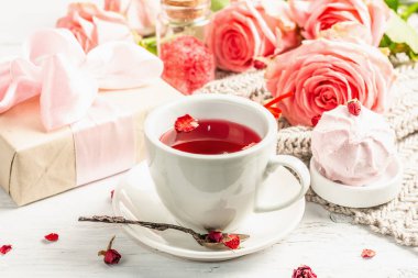 Romantik çay kavramı. Paketlenmiş hediye, amber çayı, bir buket narin gül, şeker, şenlikli dekor. Sevgililer Günü konsepti, Kadınlar Günü 8 Mart, Düğün. Beyaz tahta arkaplanı, kapat
