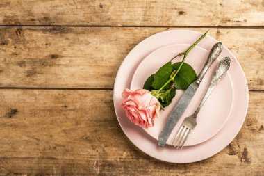 Ahşap kırsal arka planda romantik yemek masası. Sevgililer günü ya da anneler günü için aşk konsepti, düğün çatal bıçak takımı. Narin pembe gül, kaliteli masa ayarları, üst manzara.