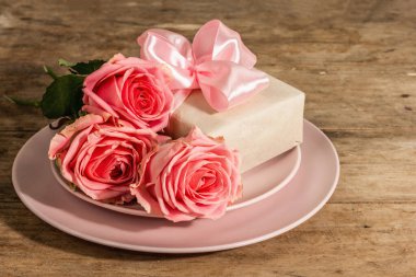 Ahşap kırsal arka planda romantik yemek masası. Sevgililer günü ya da anneler günü için aşk konsepti, düğün çatal bıçak takımı. Narin pembe güller, hediye, kaliteli masa ayarları, kapat.