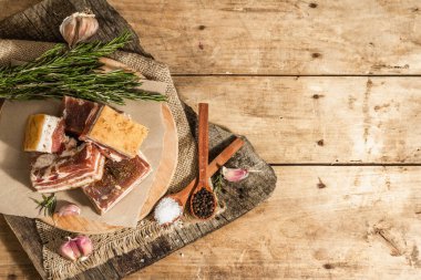 Baharatla pişirilmiş tuzlu, yüksek yağlı et parçaları. Salo, pastırma, domuz yağı, gümüş, tavla. Sarımsak, taze biberiye, baharatlar. Sert ışık, karanlık gölge, ahşap arka plan, üst manzara
