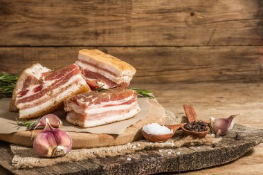 Baharatla pişirilmiş tuzlu, yüksek yağlı et parçaları. Salo, pastırma, domuz yağı, gümüş, tavla. Sarımsak, taze biberiye, baharatlar. Sert ışık, karanlık gölge, ahşap arkaplan, kopyalama alanı