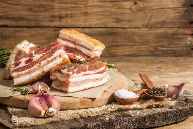 Baharatla pişirilmiş tuzlu, yüksek yağlı et parçaları. Salo, pastırma, domuz yağı, gümüş, tavla. Sarımsak, taze biberiye, baharatlar. Sert ışık, karanlık gölge, ahşap arkaplan, kopyalama alanı