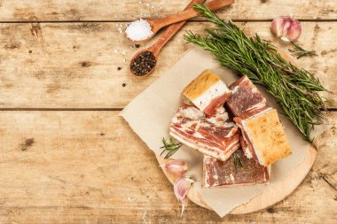 Baharatla pişirilmiş tuzlu, yüksek yağlı et parçaları. Salo, pastırma, domuz yağı, gümüş, tavla. Sarımsak, taze biberiye, baharatlar. Sert ışık, karanlık gölge, ahşap arka plan, üst manzara