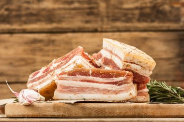 Baharatla pişirilmiş tuzlu, yüksek yağlı et parçaları. Salo, pastırma, domuz yağı, gümüş, tavla. Sarımsak, taze biberiye, baharatlar. Sert ışık, karanlık gölge, ahşap arkaplan, kopyalama alanı