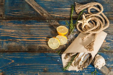 Kağıt bir pakette güneşte kurutulmuş eritilmiş. Deniz dekorlu tuzlu balık. Limon, taze biberiye, deniz ipi. Mavi denizcilik ahşap arka plan, üst görünüm