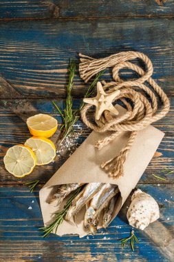 Kağıt bir pakette güneşte kurutulmuş eritilmiş. Deniz dekorlu tuzlu balık. Limon, taze biberiye, deniz ipi. Mavi denizcilik ahşap arka plan, üst görünüm