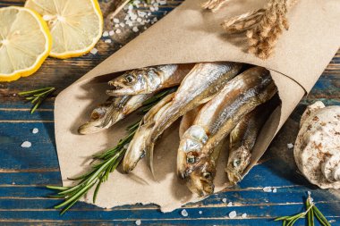 Kağıt bir pakette güneşte kurutulmuş eritilmiş. Deniz dekorlu tuzlu balık. Limon, taze biberiye, deniz ipi. Mavi denizcilik ahşap arka plan, kapat