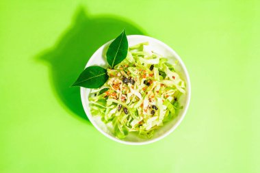 Bahar diyeti salatası. Taze vejetaryen vitamin yiyeceği. Dilimlenmiş lahana, baharat, zeytinyağı, kuru böğürtlen. Sağlıklı yaşam tarzı kavramı. Modaya uygun sert ışık, koyu gölge, parlak yeşil arkaplan, üst manzara