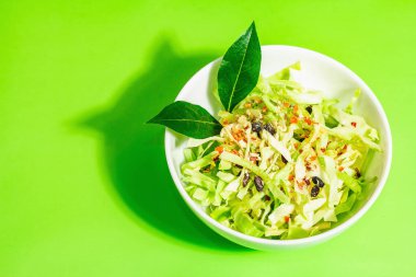 Bahar diyeti salatası. Taze vejetaryen vitamin yiyeceği. Dilimlenmiş lahana, baharat, zeytinyağı, kuru böğürtlen. Sağlıklı yaşam tarzı kavramı. Modaya uygun sert ışık, koyu gölge, parlak yeşil arkaplan, üst manzara