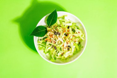 Bahar diyeti salatası. Taze vejetaryen vitamin yiyeceği. Dilimlenmiş lahana, baharat, zeytinyağı, kuru böğürtlen. Sağlıklı yaşam tarzı kavramı. Modaya uygun sert ışık, koyu gölge, parlak yeşil arkaplan, üst manzara