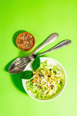 Bahar diyeti salatası. Taze vejetaryen vitamin yiyeceği. Dilimlenmiş lahana, baharat, zeytinyağı, kuru böğürtlen. Sağlıklı yaşam tarzı kavramı. Modaya uygun sert ışık, koyu gölge, parlak yeşil arkaplan, üst manzara