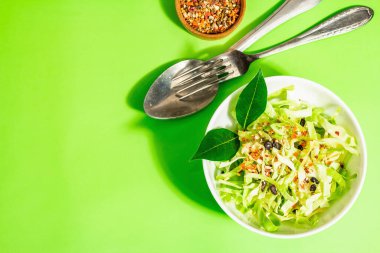 Bahar diyeti salatası. Taze vejetaryen vitamin yiyeceği. Dilimlenmiş lahana, baharat, zeytinyağı, kuru böğürtlen. Sağlıklı yaşam tarzı kavramı. Modaya uygun sert ışık, koyu gölge, parlak yeşil arkaplan, üst manzara