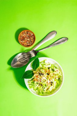 Bahar diyeti salatası. Taze vejetaryen vitamin yiyeceği. Dilimlenmiş lahana, baharat, zeytinyağı, kuru böğürtlen. Sağlıklı yaşam tarzı kavramı. Modaya uygun sert ışık, koyu gölge, parlak yeşil arkaplan, üst manzara