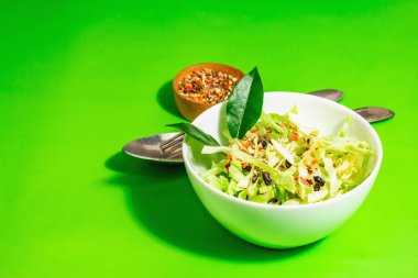 Bahar diyeti salatası. Taze vejetaryen vitamin yiyeceği. Dilimlenmiş lahana, baharat, zeytinyağı, kuru böğürtlen. Sağlıklı yaşam tarzı kavramı. Modaya uygun sert ışık, koyu gölge, parlak yeşil arkaplan, kopyalama alanı
