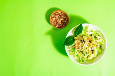 Bahar diyeti salatası. Taze vejetaryen vitamin yiyeceği. Dilimlenmiş lahana, baharat, zeytinyağı, kuru böğürtlen. Sağlıklı yaşam tarzı kavramı. Modaya uygun sert ışık, koyu gölge, parlak yeşil arkaplan, üst manzara
