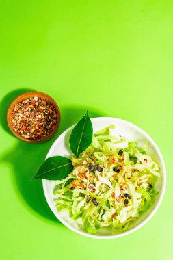 Bahar diyeti salatası. Taze vejetaryen vitamin yiyeceği. Dilimlenmiş lahana, baharat, zeytinyağı, kuru böğürtlen. Sağlıklı yaşam tarzı kavramı. Modaya uygun sert ışık, koyu gölge, parlak yeşil arkaplan, üst manzara